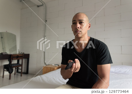 Man sitting and watching television at home while sitting on bed Man sitting and watching television at home while sitting on bed 129773464