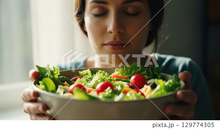 Young woman with closed eyes enjoying the fresh aroma of a healthy green salad bowl 129774305