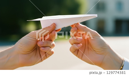 Man and woman hands holding a white paper airplane, ready for launch outdoors Man and woman hands holding a white paper airplane, ready for launch outdoors 129774381