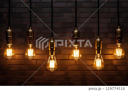 Vintage light bulbs hang on a rustic brick wall, creating a warm and cozy atmosphere. The soft light of the bulbs contrasts with the rough texture of the exposed brick, giving the room personality. 129774518