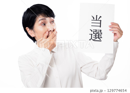 当選と書かれた紙を持ち驚くシニア女性 当選と書かれた紙を持ち驚くシニア女性 129774654