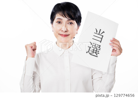 当選と書かれた紙を持ち笑顔でガッツポーズをするシニア女性 129774656