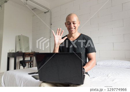Remote work from home concept bald man sitting on bed using laptop computer for video call meeting 129774966