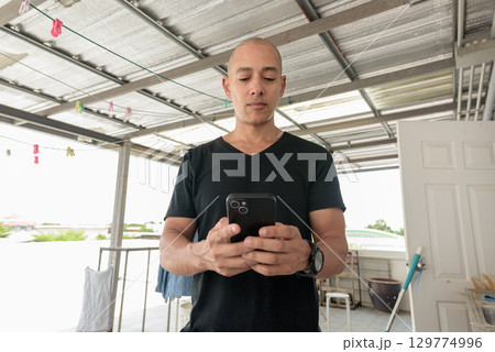 Hispanic bald man using phone while doing laundry outdoors during day Hispanic bald man using phone while doing laundry outdoors during day 129774996