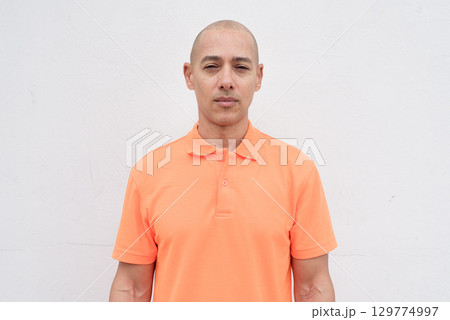 Bald Italian man in orange polo shirt studio portrait against white wall Bald Italian man in orange polo shirt studio portrait against white wall 129774997