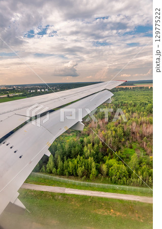 View of airplane wing, blue skies and green land during landing. Airplane window view. 129775222