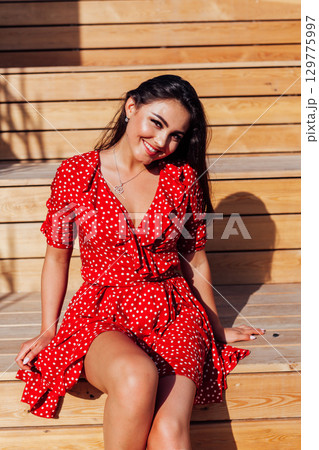 Stylish girl in summer outfit: , red dress, white bag walk on old city streets 129775997