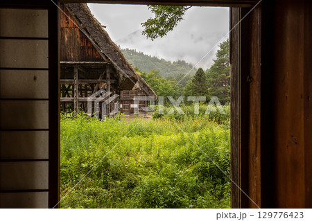雨の中、家の中から見た白川郷の古民家と山の風景 雨の中、家の中から見た白川郷の古民家と山の風景 129776423