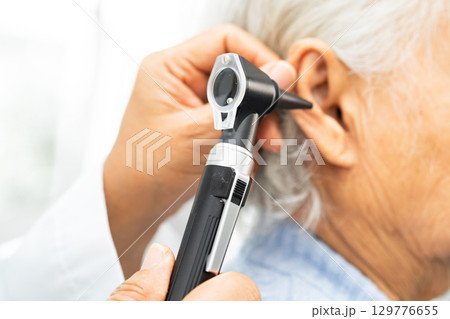 Audiologist or ENT doctor use otoscope checking ear of asian senior woman patient treating hearing loss problem. Audiologist or ENT doctor use otoscope checking ear of asian senior woman patient treating hearing loss problem. 129776655