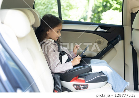 Cute school-aged girl sitting in a car with her seatbelt fixed 129777315