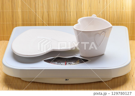 Empty plate saucer and mug cup on weighing scale. Empty plate saucer and mug cup on weighing scale. 129780127