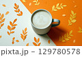 Cup of frothy coffee on orange and cream background with autumn-themed paper cut leaves 129780578
