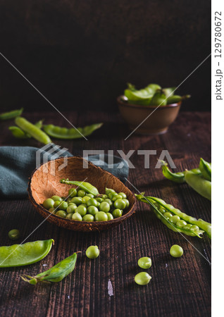 Fresh green peas in a bowl and in pods on the table vertical view 129780672