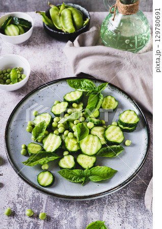 Green vegetarian salad with cucumbers, peas and basil on a plate on the table vertical view 129780691