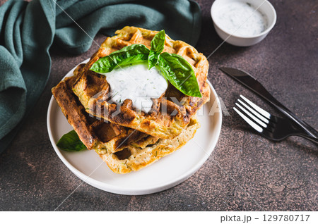 Zucchini waffles with spices, sour cream and herbs on a plate on the table 129780717
