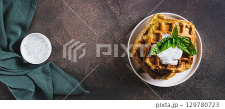 Zucchini waffles with spices, sour cream and herbs on a plate top view web banner 129780723