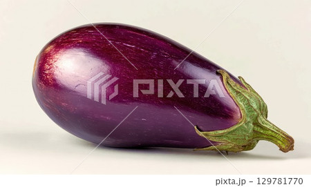 A large, deep purple eggplant with a green stem is placed on a simple white background in a studio setting 129781770