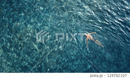 A solo swimmer glides peacefully through the crystalline turquoise water of a tropical ocean or sea A solo swimmer glides peacefully through the crystalline turquoise water of a tropical ocean or sea 129782107