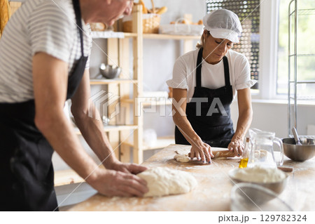 Elderly man and woman knead and roll out dough Elderly man and woman knead and roll out dough 129782324