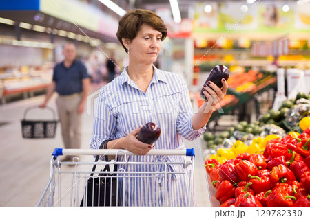 mature woman choosing eggplant in supermarket mature woman choosing eggplant in supermarket 129782330