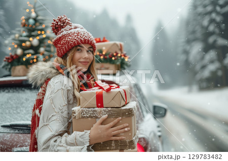 Woman holding Christmas gifts standing near red car with decorated tree in snowy winter forest Woman holding Christmas gifts standing near red car with decorated tree in snowy winter forest 129783482