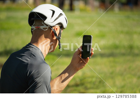 Male cyclist holding smartphone with empty blank screen on bike at park. Male cyclist holding smartphone with empty blank screen on bike at park. 129785388