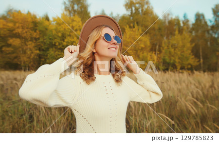 Happy young woman enjoying warm sunny weather in autumn park outdoors 129785823