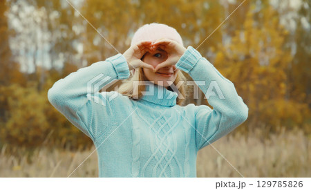 Portrait of happy young woman showing heart shaped sign gesture with hands in autumn park 129785826