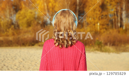 Inspired young woman enjoying listening to music in headphones outdoors in autumn forest Inspired young woman enjoying listening to music in headphones outdoors in autumn forest 129785829