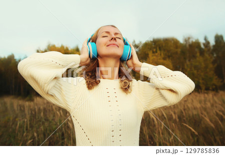Inspired young woman enjoying listening to music in headphones outdoors in autumn forest Inspired young woman enjoying listening to music in headphones outdoors in autumn forest 129785836