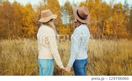 Two women friends together in autumn park, stylish girlfriends in hat, trees with yellow leaves Two women friends together in autumn park, stylish girlfriends in hat, trees with yellow leaves 129786060