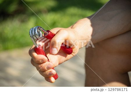 Man strengthens his grip using hand red metal expander. He is seen holding expander with firm grip, suggesting focused exercise 129786171