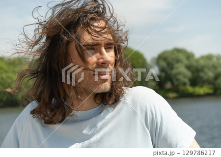 Man with long curly hair wearing casual blue and sunglasses gazes up on cloudy blue sky. Casual blue tshirt complements serene, thoughtful expression. Banner. Summer. Background for reflection. 129786217