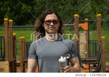 Man relaxed in park holding water bottle Man relaxed in park holding water bottle 129786226