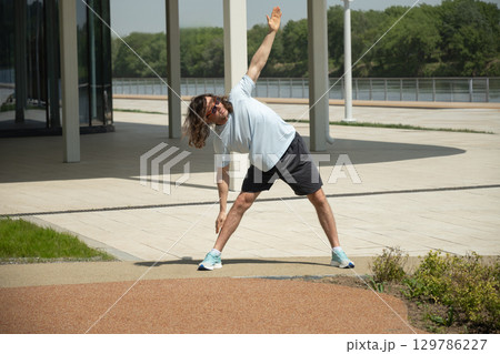 Fit man doing warm up exercise on city modern public park. Summer activity Fit man doing warm up exercise on city modern public park. Summer activity 129786227