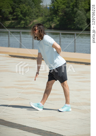 Fit man doing warm up exercise on city modern public park. Summer activity 129786228