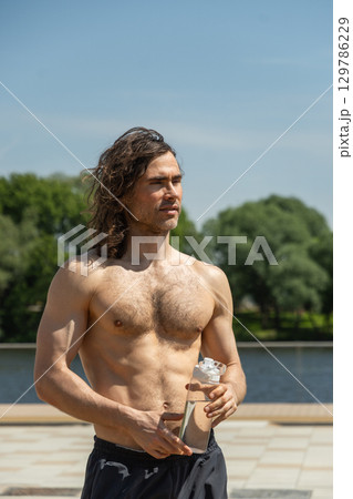 Shirtless young man holding water bottle. Outdoors. Summer. 129786229