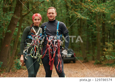 Standing and posing. Man and woman doing climbing in forest with use of safety equipment 129786574