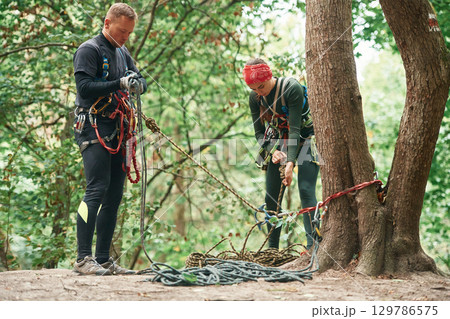 Man and woman doing climbing in forest with use of safety equipment 129786575