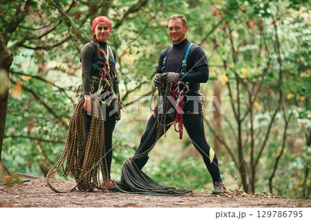 Standing and posing. Man and woman doing climbing in forest with use of safety equipment 129786795
