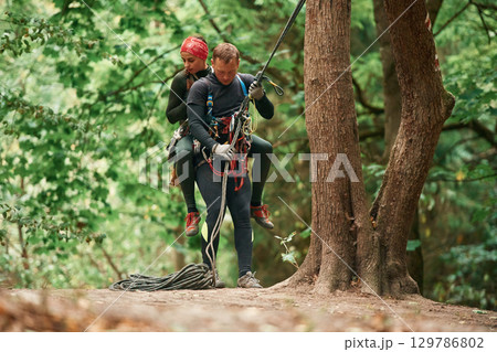 Going down. Man and woman doing climbing in forest with use of safety equipment 129786802