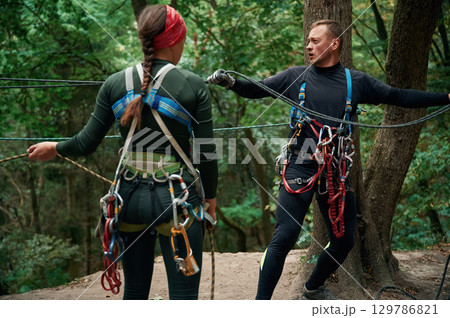In the forest. Man and woman doing climbing with use of safety equipment In the forest. Man and woman doing climbing with use of safety equipment 129786821