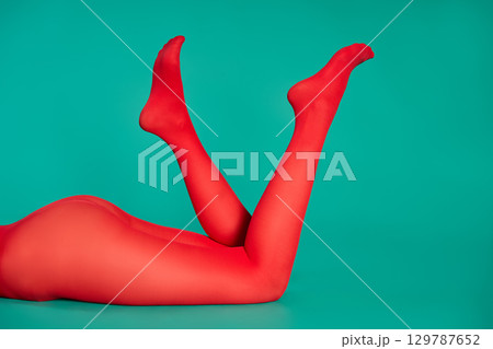 Long legs of beautiful young woman in bright red tights relax on green background Long legs of beautiful young woman in bright red tights relax on green background 129787652