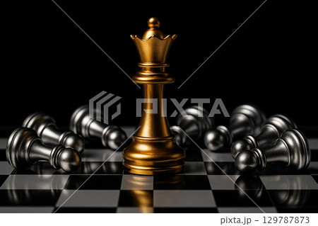 A golden king chess piece standing victorious among fallen black pieces representing ultimate leadership power and triumph A golden king chess piece standing victorious among fallen black pieces representing ultimate leadership power and triumph 129787873