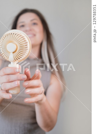 Summer lifestyle concept happy young woman cooling off with a personal mini gadget for instant comfort outdoors. 129788351
