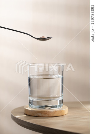 A spoon of Himalayan salt is being added to a glass of drinking water. 129788893