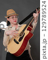 Playful woman guitarist strumming classical six string acoustic guitar. Candid woman musician wearing eyeglasses, dressed in chic leather jacket and stylish straw hat, adds to lively atmosphere 129789524