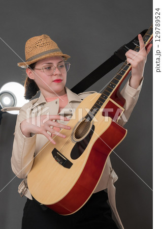 Playful woman guitarist strumming classical six string acoustic guitar. Candid woman musician wearing eyeglasses, dressed in chic leather jacket and stylish straw hat, adds to lively atmosphere Playful woman guitarist strumming classical six string acoustic guitar. Candid woman musician wearing eyeglasses, dressed in chic leather jacket and stylish straw hat, adds to lively atmosphere 129789524
