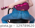 Rear view of sitting female musician holding ukulele behind her back. Sexy unrecognizable woman in blue tight jeans that hugs her figure. Back view of midsection female body holding musical instrument 129789620