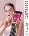 Young woman musician holding her ukulele and tuning strings of musical instrument, tightening and loosening strings before beginning to play ukulele. Daily routine of ukulele tuning. Selective focus 129789621